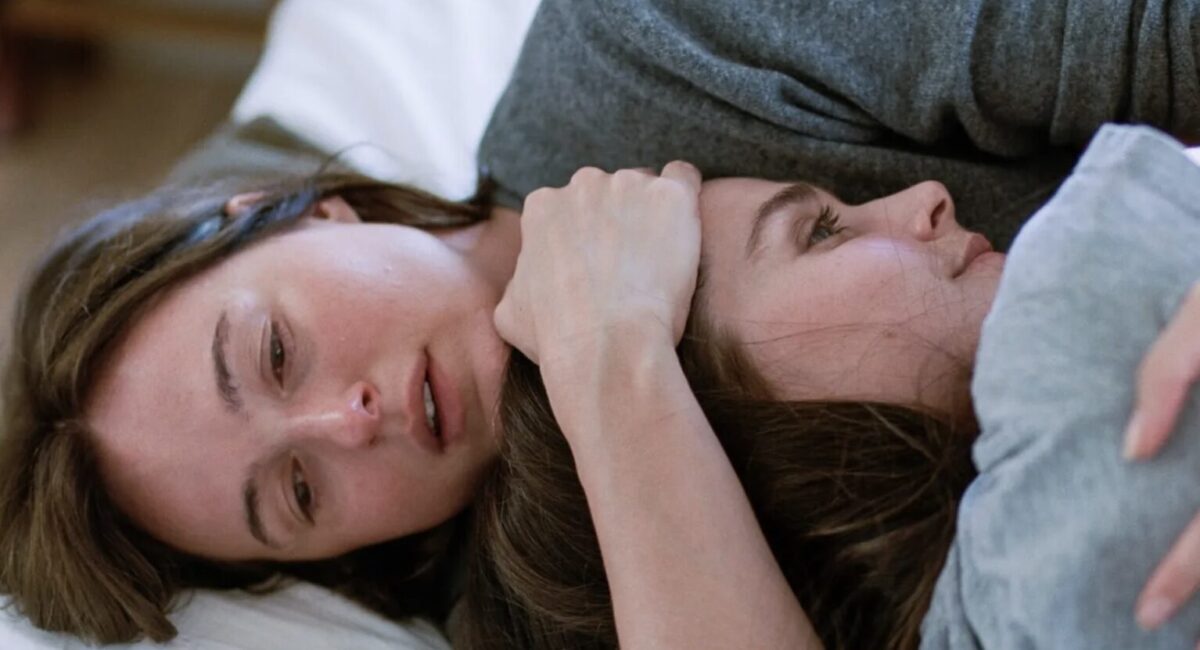 A crying woman holds another while lying down